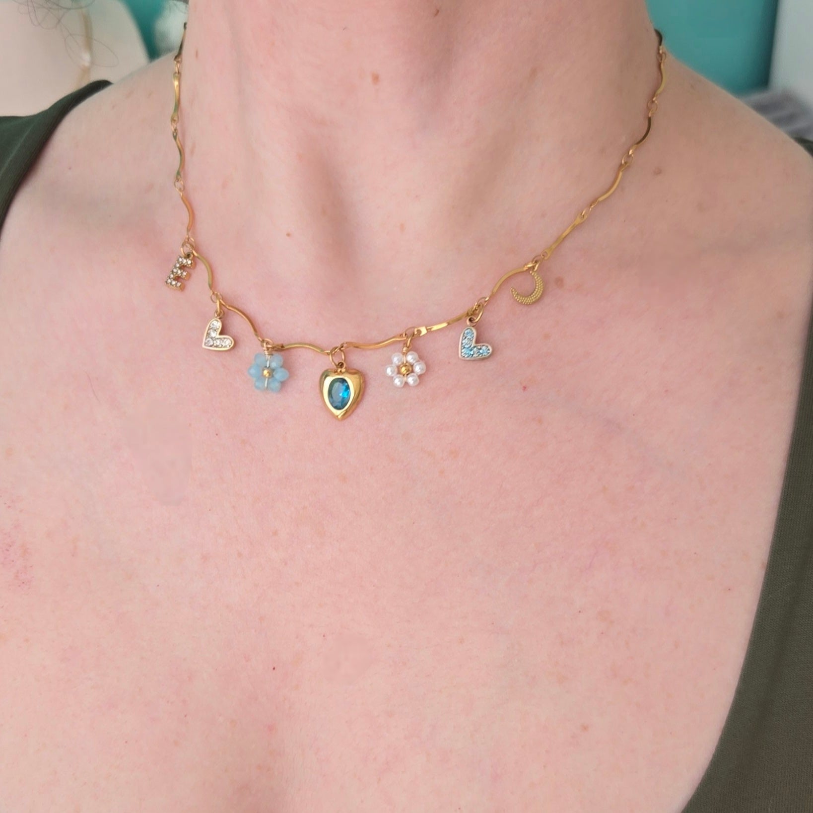 Necklace with heart and flower charms on a person wearing a green top.